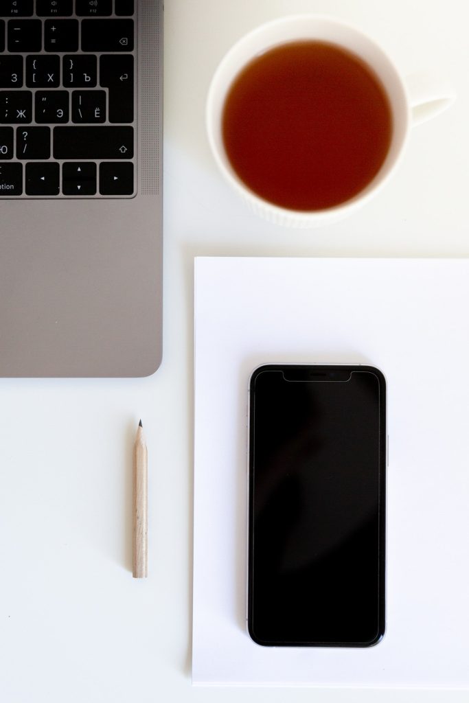 Cup of tea near laptop keyboard with smartphone on paper and wooden pencil